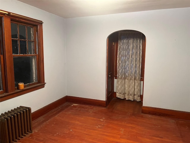 spare room with radiator, arched walkways, baseboards, and wood finished floors