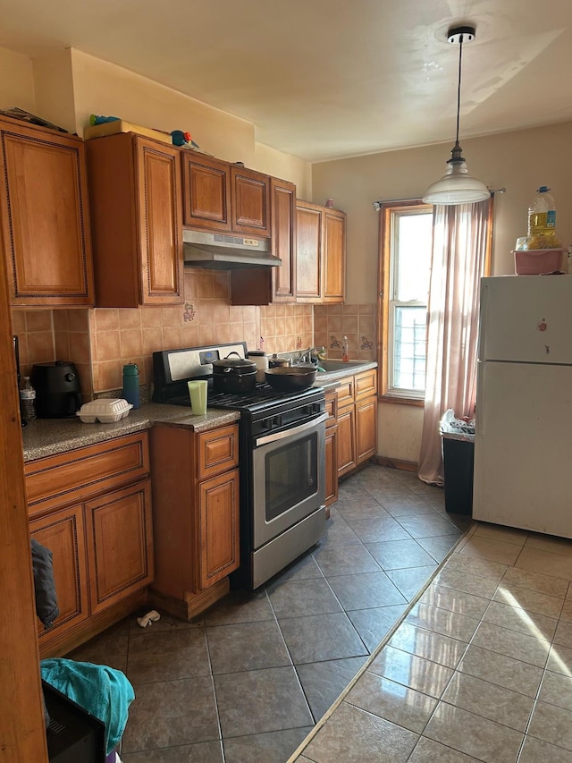 45 S Lander St, Newburgh, NY 12550 - kitchen featuring freestanding refrigerator, stainless steel gas range oven, under cabinet range hood, backsplash, and brown cabinets