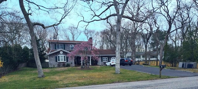 traditional-style house with aphalt driveway, fence, a front lawn, and a chimney