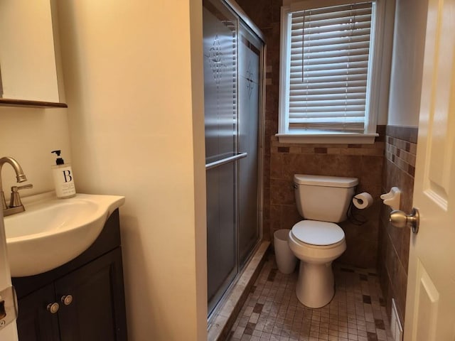 bathroom featuring toilet, tile walls, vanity, a stall shower, and wainscoting