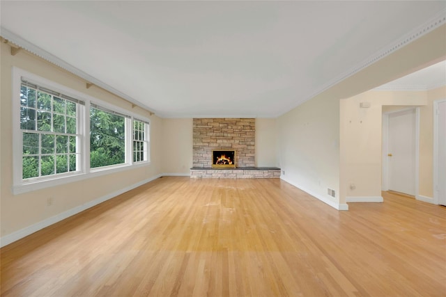 unfurnished living room featuring visible vents, baseboards, a stone fireplace, light wood-style floors, and ornamental molding