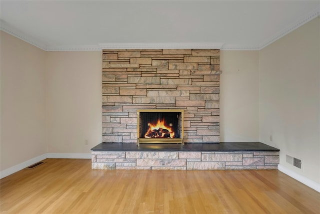 interior details with a stone fireplace, visible vents, crown molding, and wood finished floors