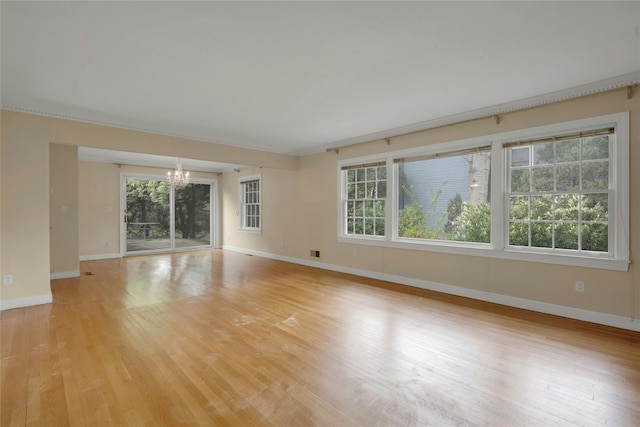 empty room with baseboards, light wood finished floors, a chandelier, and plenty of natural light