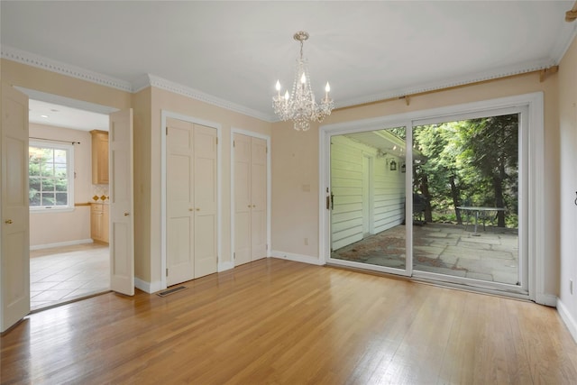 unfurnished bedroom with a notable chandelier, light wood-style flooring, visible vents, two closets, and access to exterior