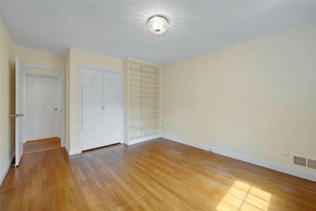 unfurnished bedroom with a closet, wood finished floors, visible vents, and baseboards