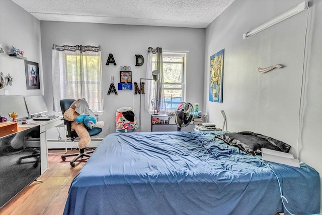 bedroom with a textured ceiling, baseboard heating, and wood finished floors