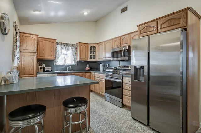 kitchen with visible vents, a kitchen bar, glass insert cabinets, dark countertops, and appliances with stainless steel finishes