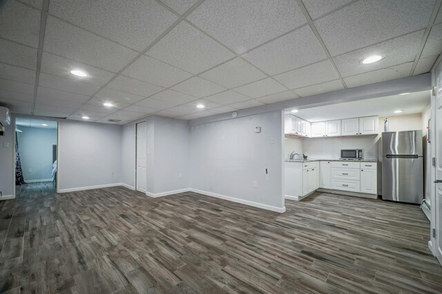 finished basement featuring freestanding refrigerator, baseboards, a sink, and dark wood-style floors