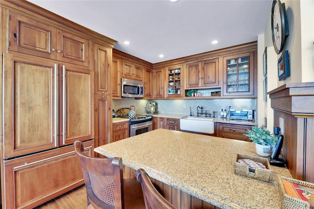 279 Dune Rd Unit 2, Westhampton Beach, NY 11978 - kitchen with appliances with stainless steel finishes, a sink, brown cabinets, decorative backsplash, and glass insert cabinets