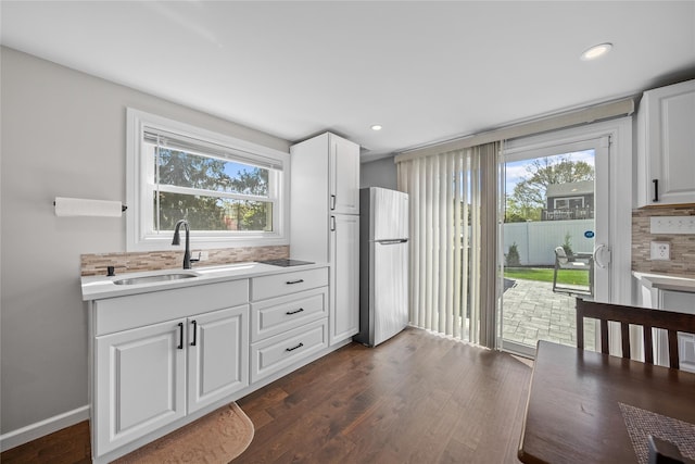 kitchen with a sink, freestanding refrigerator, white cabinets, dark wood-type flooring, and backsplash