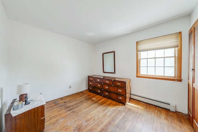 unfurnished bedroom with a closet, baseboard heating, and light wood-type flooring