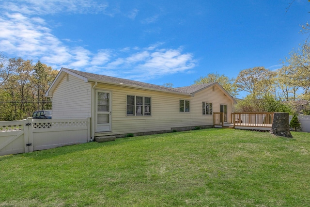 rear view of house featuring a lawn, a wooden deck, fence, and a gate
