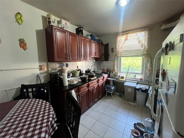 kitchen with dark brown cabinets, light tile patterned floors, a sink, backsplash, and dark countertops