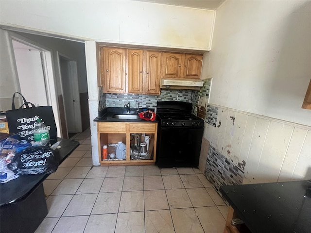 kitchen featuring black range with gas cooktop, under cabinet range hood, light tile patterned floors, backsplash, and dark countertops