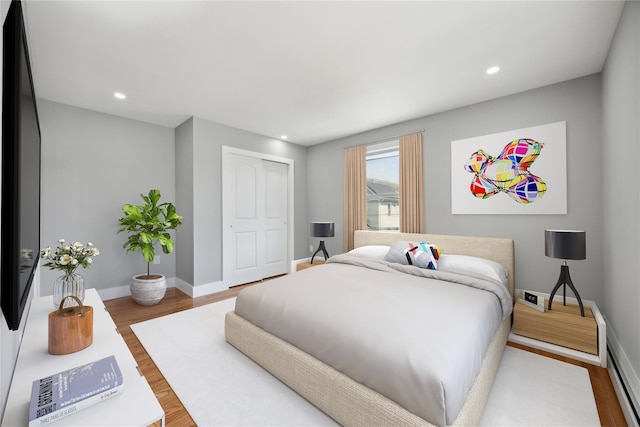 bedroom with wood finished floors, a closet, baseboards, baseboard heating, and recessed lighting