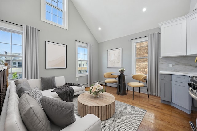 living area with light wood-style floors, high vaulted ceiling, plenty of natural light, and recessed lighting