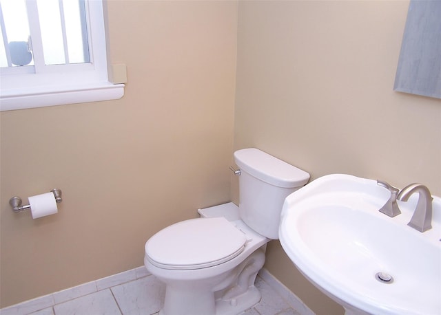 half bathroom featuring baseboards, toilet, and a sink