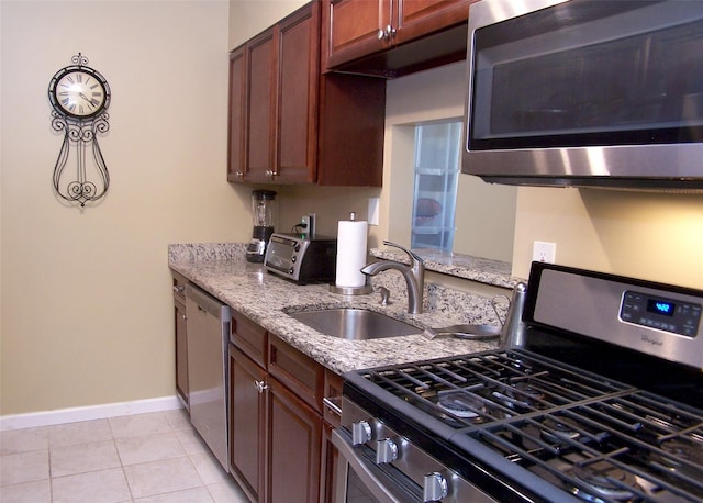 kitchen with a sink, stainless steel appliances, baseboards, light stone countertops, and light tile patterned flooring