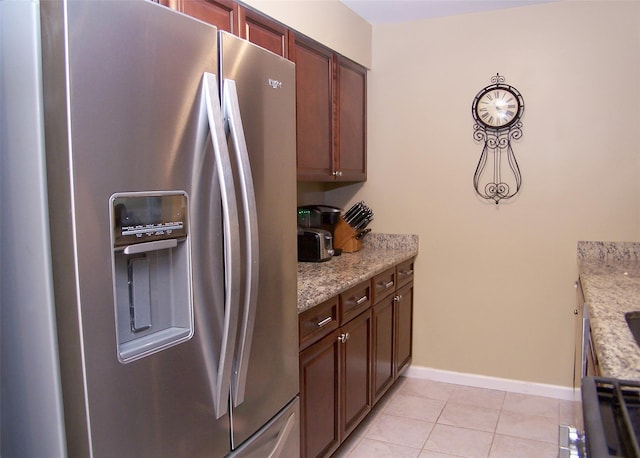 kitchen featuring light stone counters, baseboards, light tile patterned flooring, and stainless steel refrigerator with ice dispenser