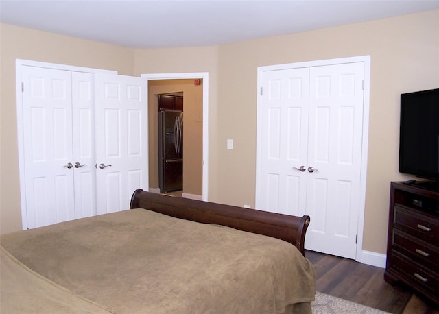 bedroom featuring baseboards, multiple closets, stainless steel fridge, and dark wood-style floors