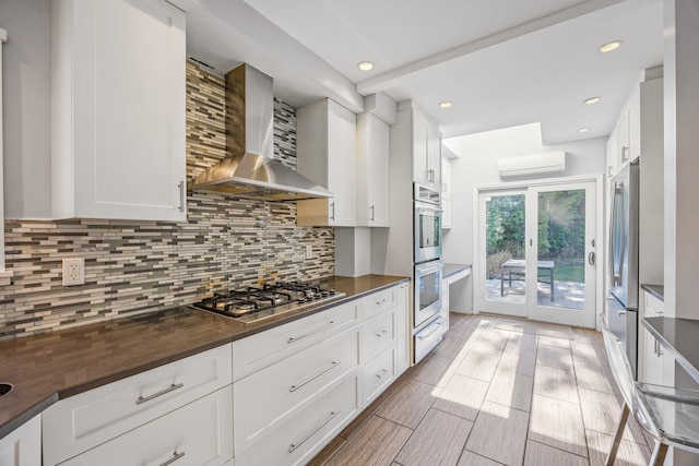 8702 Chevy Chase St, Jamaica Estates, NY 11432 - kitchen featuring wall chimney range hood, appliances with stainless steel finishes, a warming drawer, white cabinetry, and recessed lighting