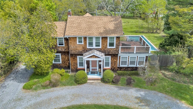 7 N Howells Point Rd, Bellport Village, NY 11713 - shingle-style home with a balcony, a chimney, roof with shingles, gravel driveway, and fence