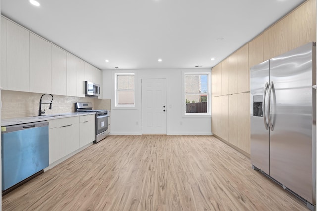 kitchen with a sink, stainless steel appliances, tasteful backsplash, light wood-type flooring, and light countertops