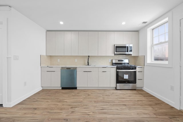 kitchen featuring light wood finished floors, stainless steel appliances, and backsplash