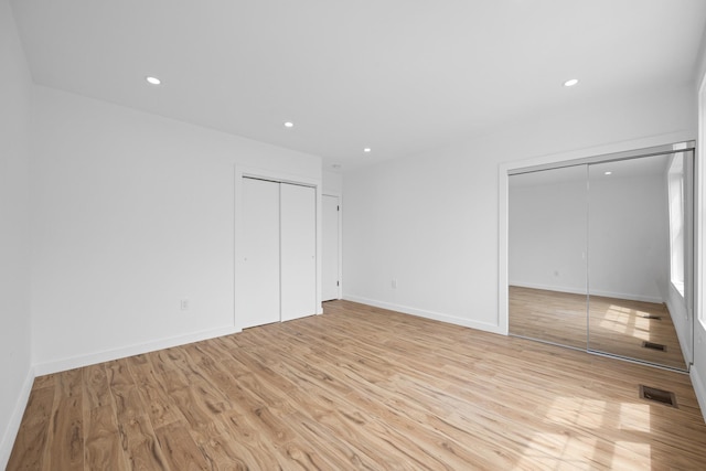 unfurnished bedroom with light wood-style flooring, recessed lighting, baseboards, visible vents, and two closets