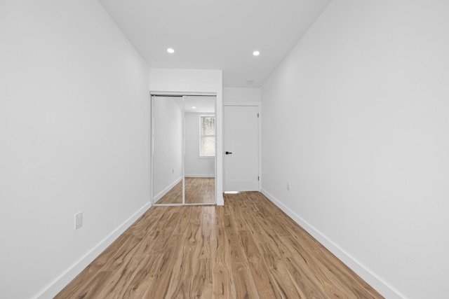 unfurnished bedroom featuring baseboards, light wood-type flooring, a closet, and recessed lighting