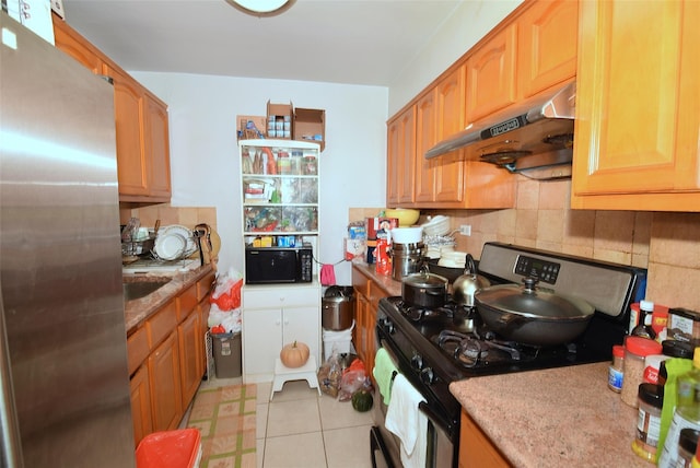 kitchen with freestanding refrigerator, gas range, under cabinet range hood, tasteful backsplash, and black microwave