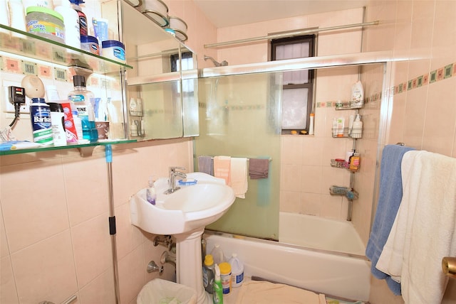 bathroom with tile walls, a sink, and shower / bath combination with glass door