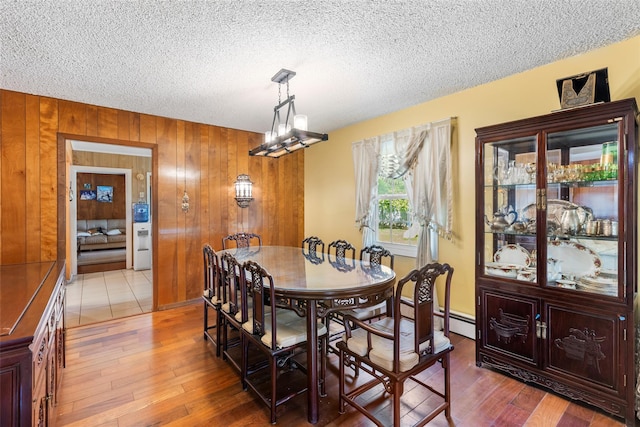 dining space with a textured ceiling, wooden walls, and light wood-style flooring
