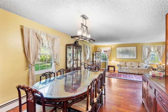 dining space with a baseboard radiator, a textured ceiling, and wood finished floors