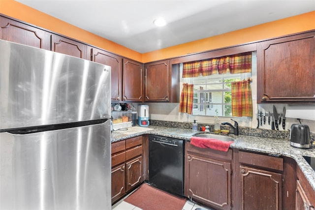 kitchen featuring freestanding refrigerator, black dishwasher, light stone counters, and a sink