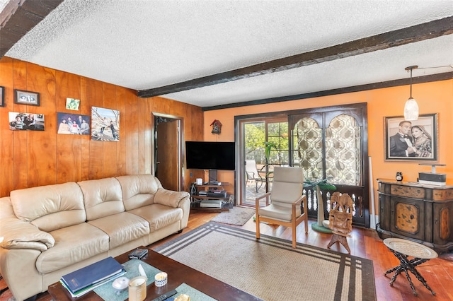 living room featuring beamed ceiling, wood walls, a textured ceiling, and wood finished floors