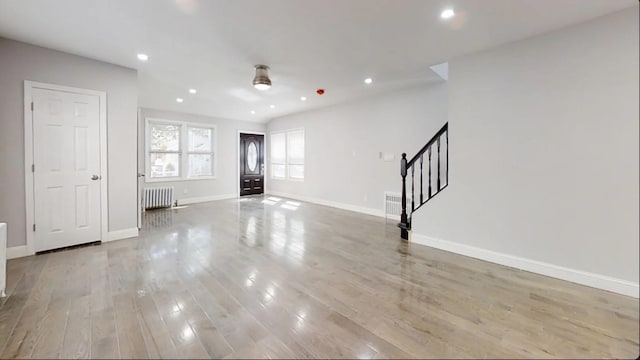 unfurnished living room with light wood-style flooring, recessed lighting, baseboards, radiator, and stairway
