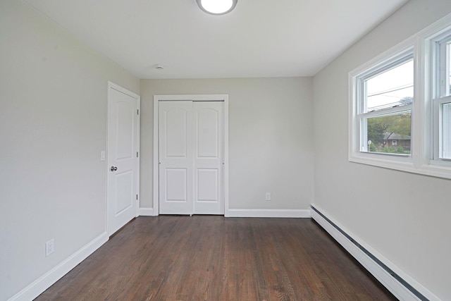 unfurnished bedroom with a baseboard radiator, dark wood-style flooring, baseboards, and a closet