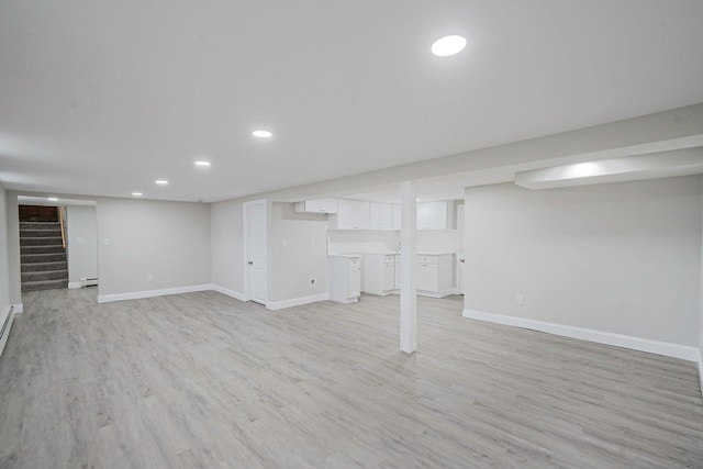 finished below grade area with a baseboard radiator, stairs, light wood finished floors, baseboards, and recessed lighting