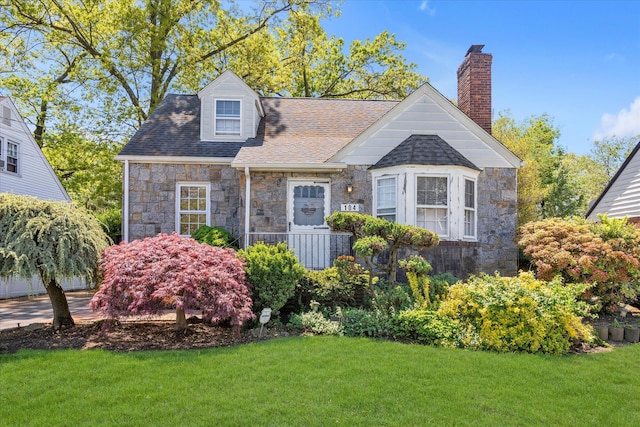 view of front of home featuring stone siding, a front lawn, a chimney, and roof with shingles