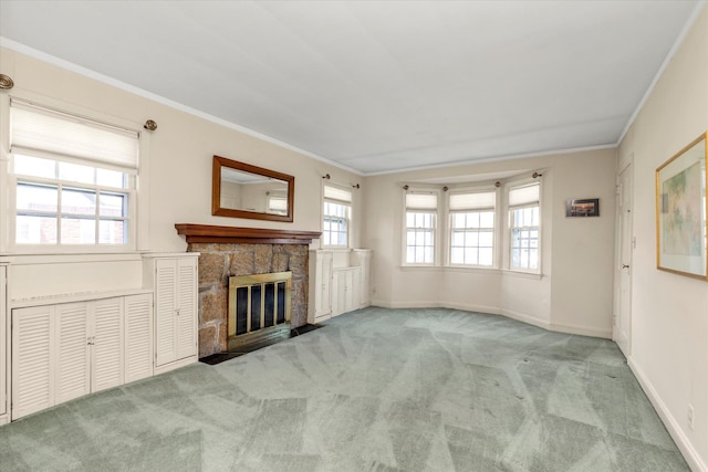unfurnished living room with carpet floors, crown molding, baseboards, and a stone fireplace