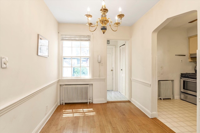 unfurnished dining area with radiator, a chandelier, light wood-style floors, and arched walkways