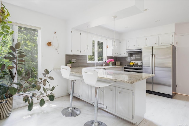 kitchen featuring stainless steel appliances, a peninsula, white cabinets, and backsplash