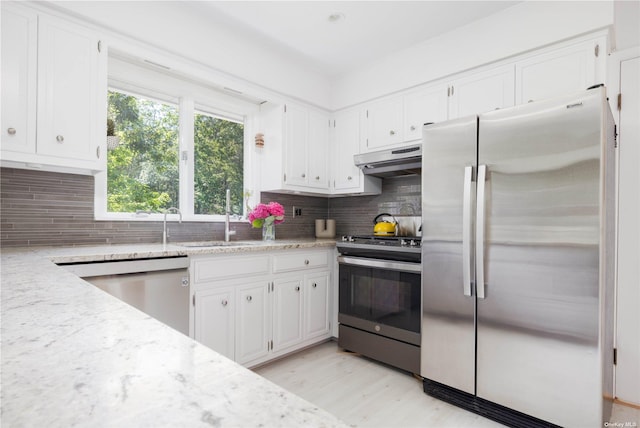 kitchen with stainless steel appliances, a sink, white cabinetry, tasteful backsplash, and light stone counters
