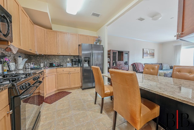 kitchen featuring visible vents, light stone counters, black appliances, and light brown cabinetry