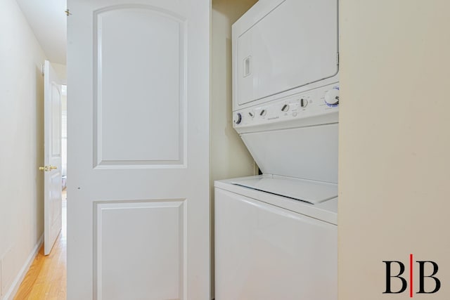 laundry area featuring laundry area, stacked washer and clothes dryer, baseboards, and light wood-type flooring
