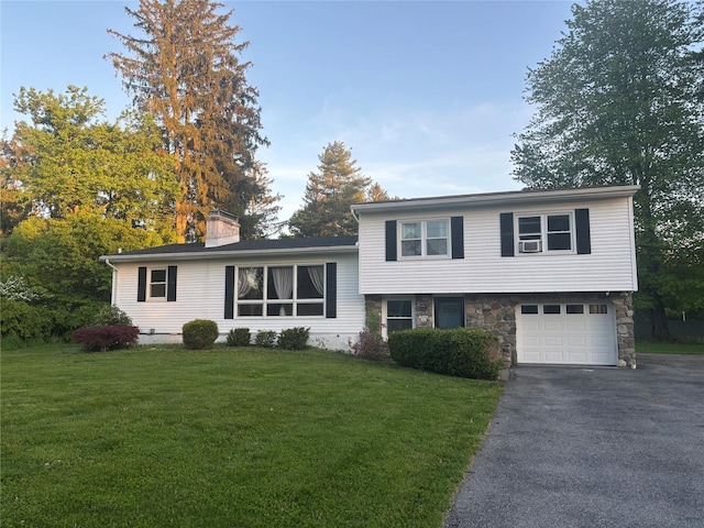 tri-level home featuring asphalt driveway, a chimney, a front lawn, and an attached garage