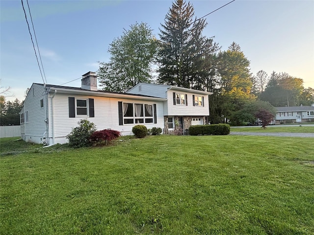 tri-level home with a chimney, an attached garage, and a front yard