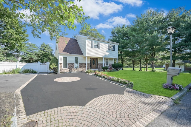 view of front of property with stone siding, a front lawn, fence, and uncovered parking