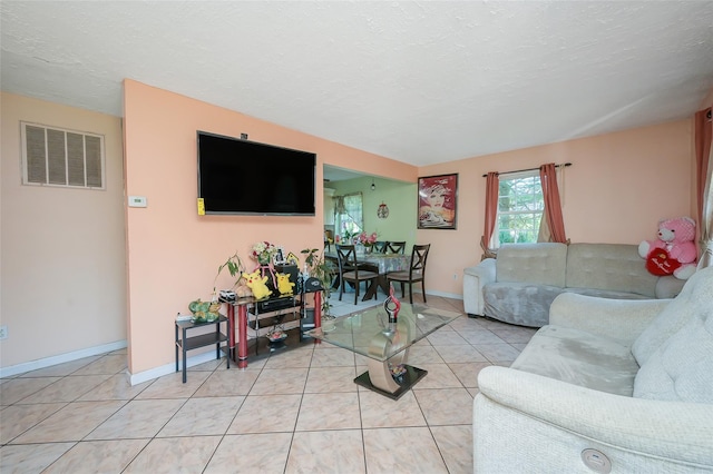 living room with light tile patterned floors, visible vents, baseboards, and a textured ceiling